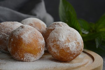 round donuts, donuts, sprinkled with powdered sugar on a round wooden board with a linen towel of gray color and a sprig of mint with copy-case