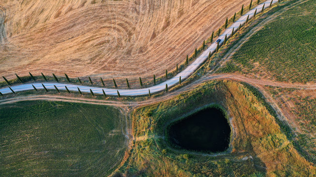 Abstract nature landscapes from drone, Tuscany, Italy. Road with cypress trees and pond.