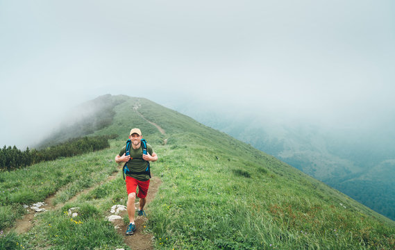 Happy hiker man walking by the cloudy and foggy weather mountain range path with backpack. Active sport backpacking healthy lifestyle concept.