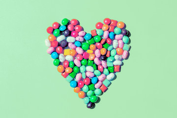 Heart shape made of small colorful candies on trendy mint background