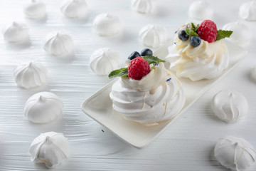 Dessert Pavlova with raspberries, blueberries and mint on a white table.