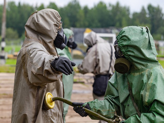 A soldier in a chemical protection suit cleans another soldier
