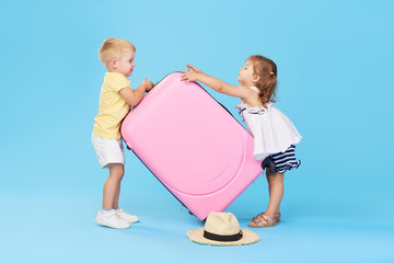 Happy kids holding colorful pink suitcase prepared for summer vacation. Young travelers. Little girl and boy, sister and brother, having fun isolated on blue background