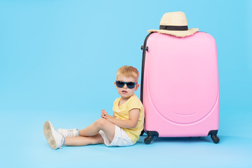 Happy child boy tourist packs clothes into a suitcase for travel, summer vacation. Toddler kid in...