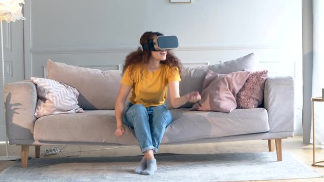 A girl in VR-glasses is moving hands and standing up