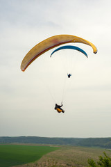 Paragliding over the green field in summer sunny day. Two paragliders fly over green field near Dnister river in Ukraine.