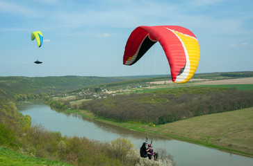 Paragliding over the green field in summer sunny day. Two paragliders fly over green field near...