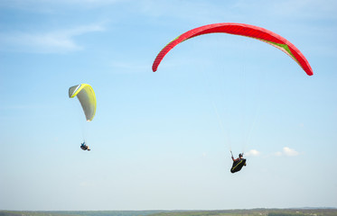 Paragliding over the green field in summer sunny day. Two paragliders fly over green field near Dnister river in Ukraine.