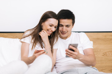 Happy laughing couple is watching media on smart phone sitting at home