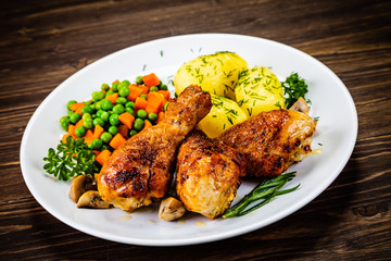 Grilled chicken drumsticks with vegetables on wooden background