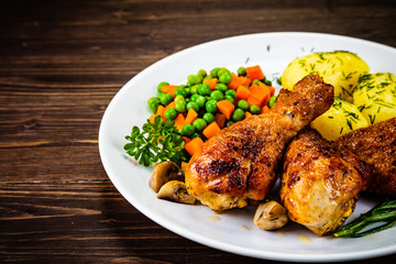 Grilled chicken drumsticks with vegetables on wooden background
