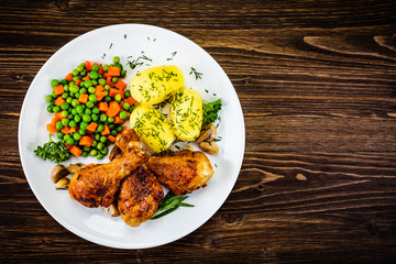 Grilled chicken drumsticks with vegetables on wooden background
