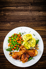 Grilled chicken drumsticks with vegetables on wooden background