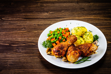 Grilled chicken drumsticks with vegetables on wooden background