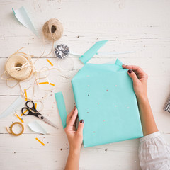 Close-up on a gift wrapped in paper of turquoise color. Hands of a young woman packing a gift on...