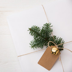 Closeup Christmas gift box wrapped in white paper and decorated with craft ribbon, bell, spruce twig and tag. A gift for the new year in on a white wooden table. Christmas concept