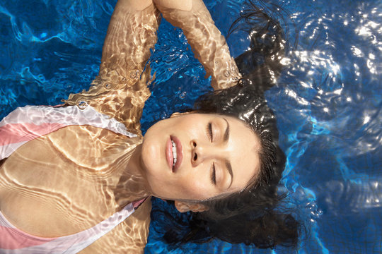 Hispanic woman floating in water in pool