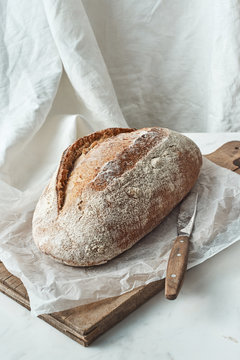 Rustic organic bread and knife on a wooden old board on a gray marble background with space for text. Top view