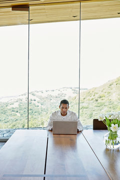 Mature African American man working on computer at dining room table at home