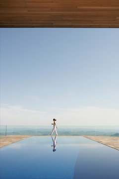 Woman walking with cup of coffee on patio with indoor / outdoor pool in foreground