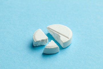 White pills on blue background. One tablet is broken in half, reducing the dose of the medicine