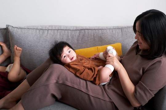 Cute Asian baby, playing in the arms of mother, on the sofa at home