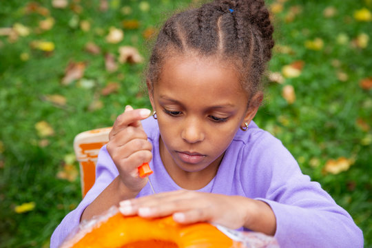 Young girl applying a stencil onto the surface of a pumpkin and attempting to carve it out