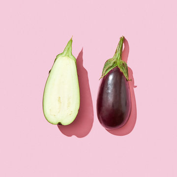 Whole and half fresh eggplant with stem on a pink background with shadow and copy space. Top view