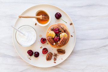 Breakfast concept. Pancakes with black cherries, bananas, pecans, yogurt and honey.
