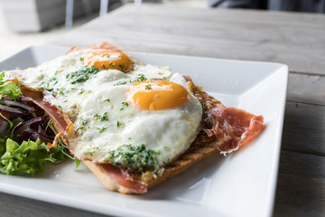 Meat sandwich with fried eggs, salad on white plate and wooden table