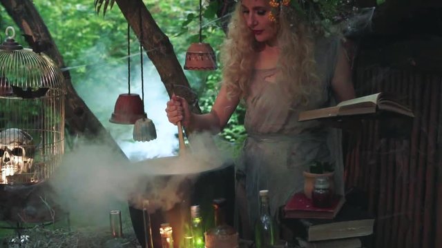 mysterious forest nymph prepares decoction of healing herbs according to recipe from magical book, woman with blond hair mixes potion with wooden spoon and blows off steam in cauldron, creative video