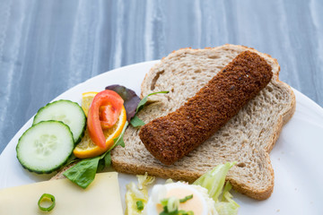 slice of brown bread with typical Dutch food called Kroket, croquette, tomato and cucumber on white plate