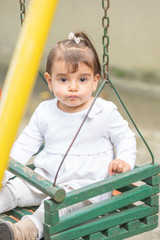 Baby girl of two have fun in the playground. She is in the seat of the swing.