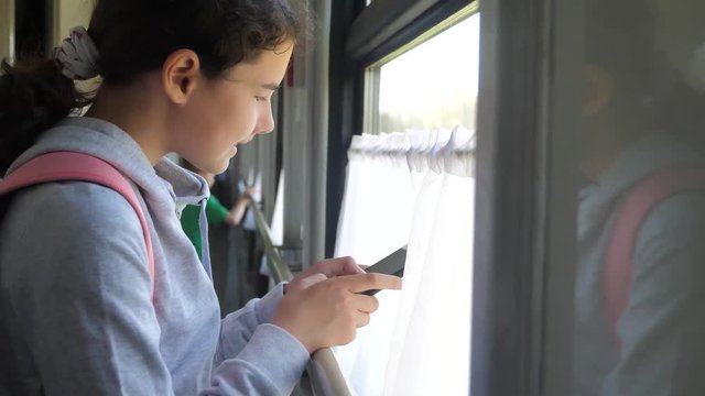 girl teenager traveler with backpack stands by the window of the train car with a smartphone. travel transportation railroad concept. the girl in lifestyle the train at the window corresponds the girl