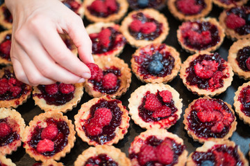 Hand of chef putting raspberry on top of cupcakes