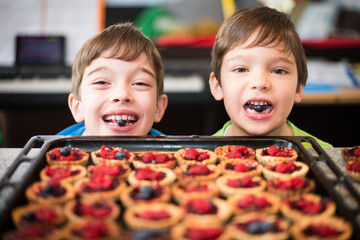 Portrait of two happy young boys helping with preparation of cupcakes