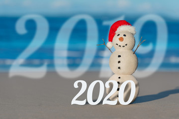 Fototapeta na wymiar Sandy Christmas Snowman on a beautiful beach at sunset with 2019 change to 2020 concept