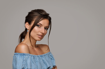 Beautiful young woman with bare shoulders with a beautiful professional evening make-up and hairstyle in a blue top with ruffles.