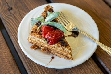 a piece of honey sponge cake decorated with strawberries and mint on a wooden table