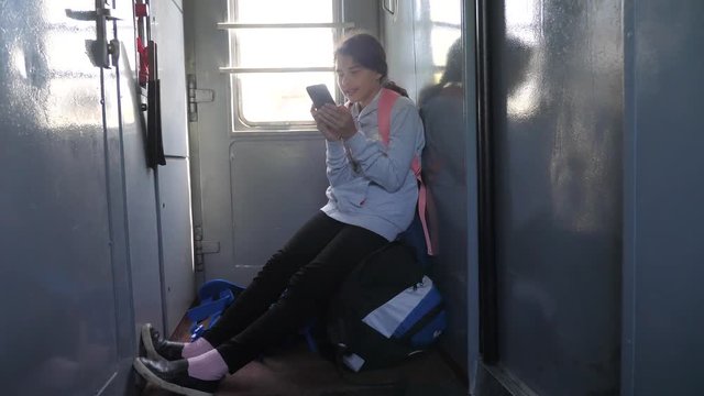 Teenager girl traveler with a backpack sitting on bags backpacks at the window of the car with a smartphone. Travel rail carriage concept. the girl in the train at the window corresponds to the girl