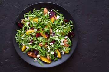 Healthy beetroot salad with oranges, arugul, feta cheese, pecans on black plate. Black background. Copy space