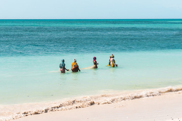 NUNGWI, Zanzibar: african women with colourful clothes on turquoise sea at Nungwi beach.