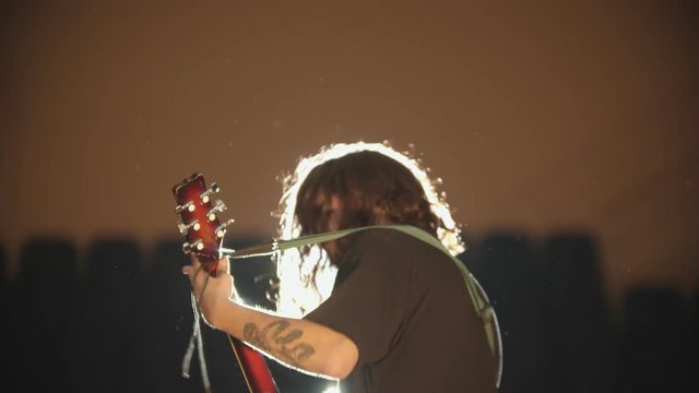 A young man with long hair playing a song at his performance and shaking his head