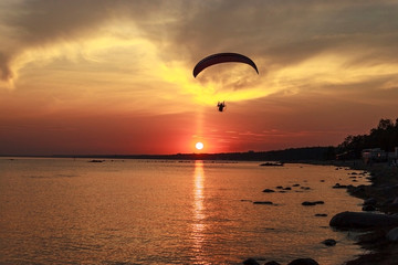 Sunset over the sea. Reflection of the sun in water. Silhouette of paraglider flying in the sky. Sunset beach in a summer evening. Gulf of Finland, Baltic sea, Komarovo, Saint-Petersburg, Russia. 