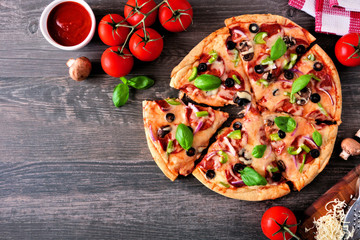 Homemade pizza with pepperoni, mushrooms, green peppers, olives, onions and basil. Top view, corner border against a wood background with copy space.