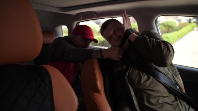 Close-up of thug suffocating man sitting in driver's seat with safety belt using it as noose. Male driver putting hand under stranglehold, unfastening seat belt and beating mugger turning to him