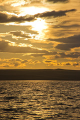 sunset, dramatic clouds, reflection of the sun in the water of the lake