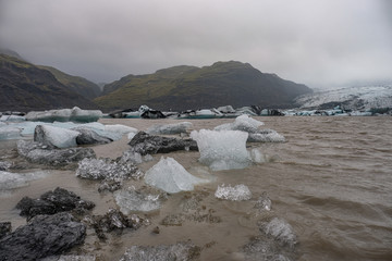 The Solheimajokull Glacier in Iceland showing icebergs and calved ice in the lagoon as ice calves...