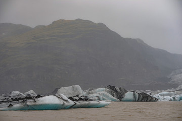 The Solheimajokull Glacier in Iceland showing icebergs and calved ice in the lagoon as ice calves...