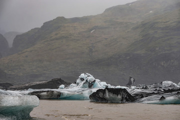 The Solheimajokull Glacier in Iceland showing icebergs and calved ice in the lagoon as ice calves...